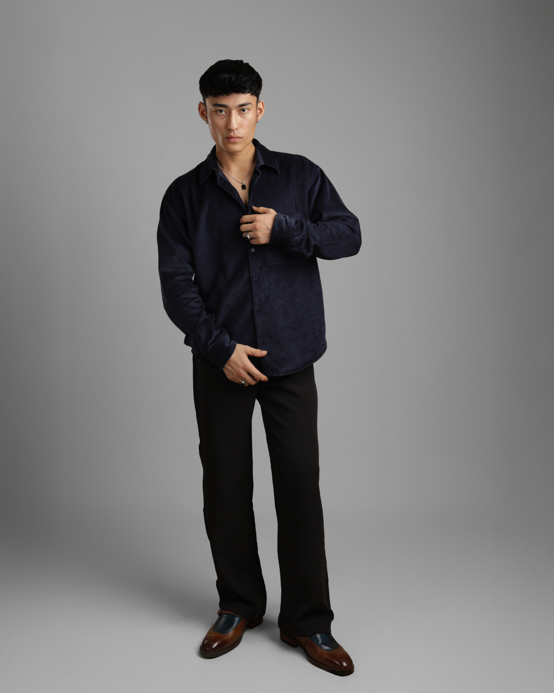 Man wearing a dark blue corduroy shirt and black pants against a gray background