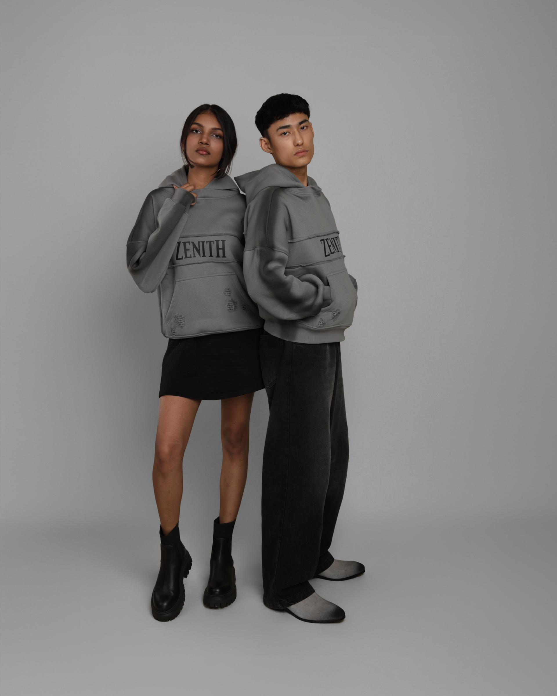 Two people wearing matching gray sweatshirts with 'Zenith' branding on a plain background