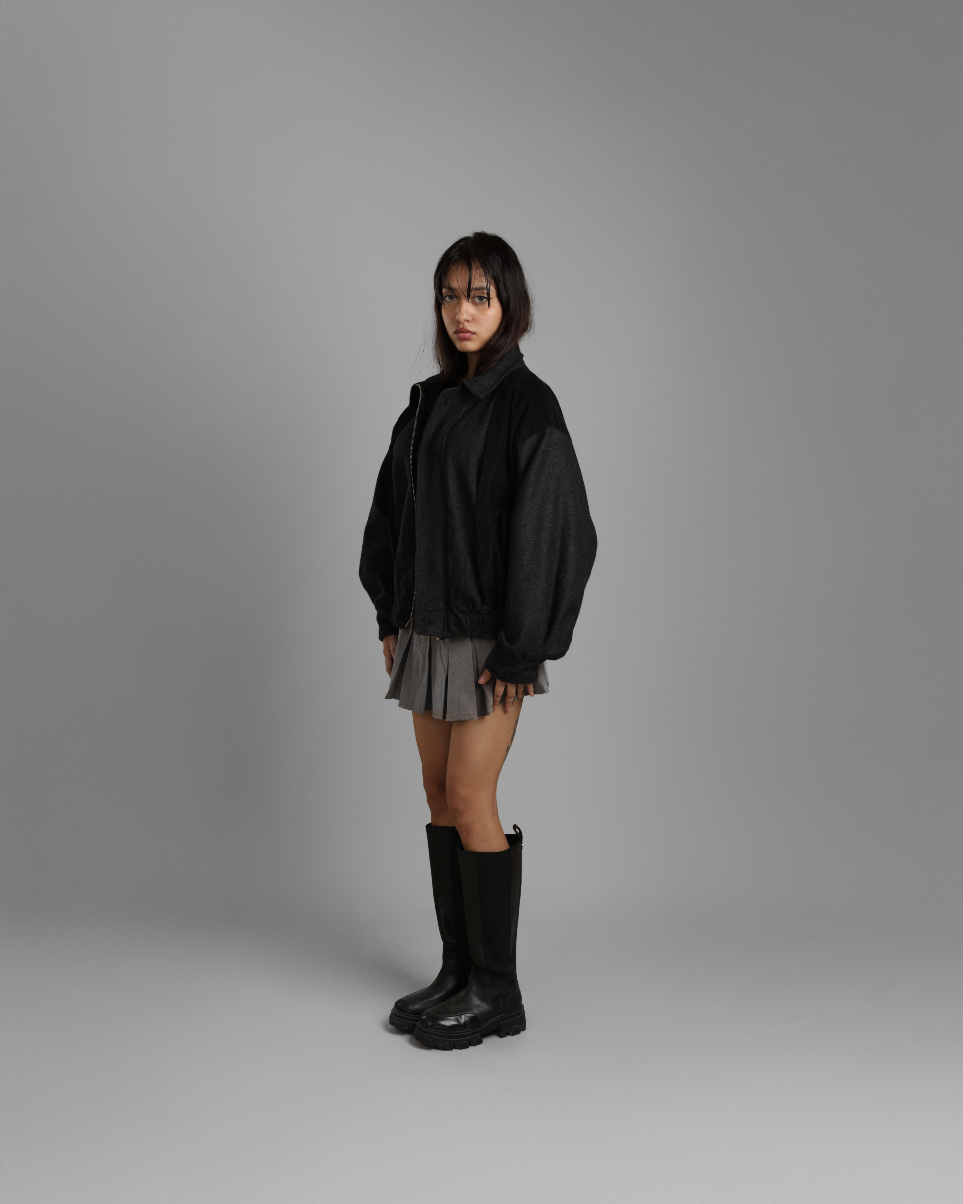 woman wearing a black grey wood corduroy zipper jacket with collar and black jeans against a gray background