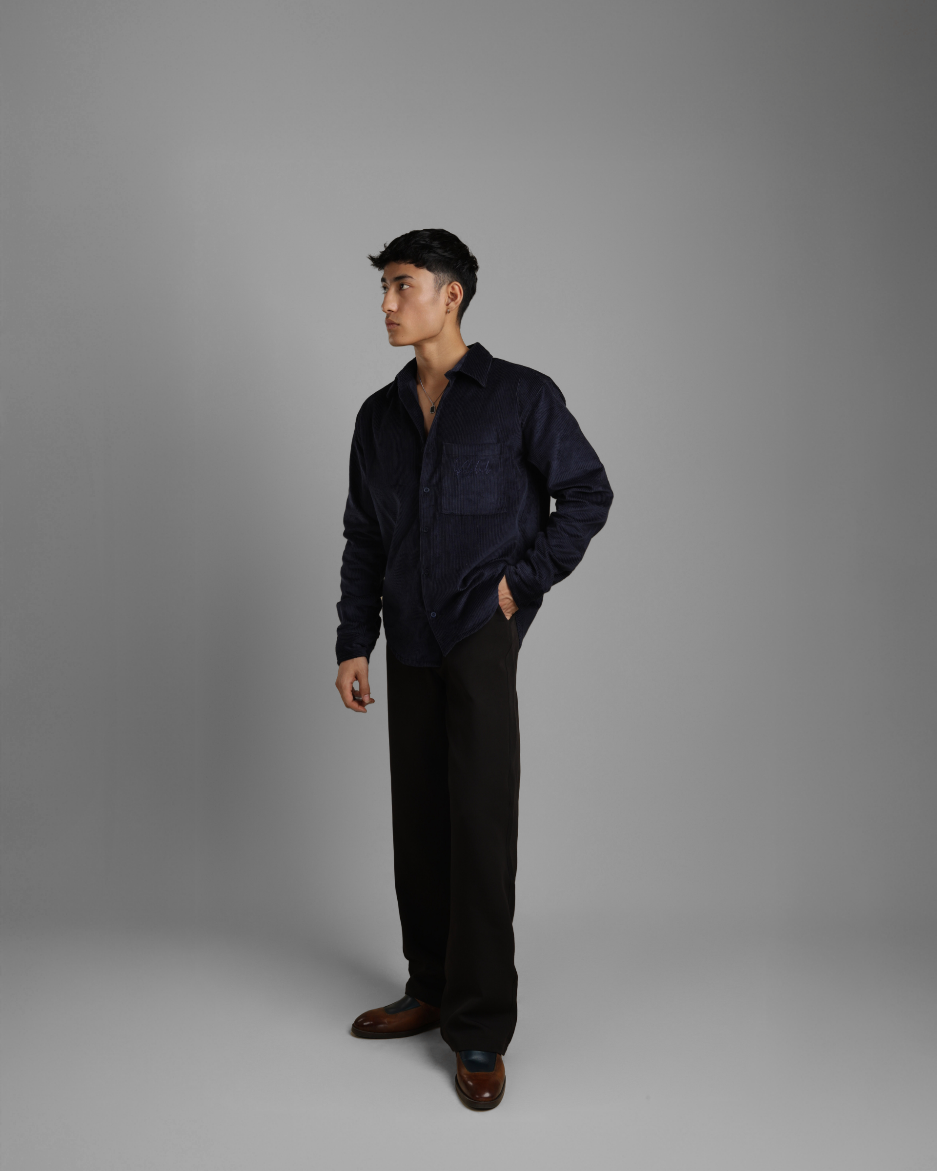 Man wearing a dark blue corduroy shirt and black pants against a gray background