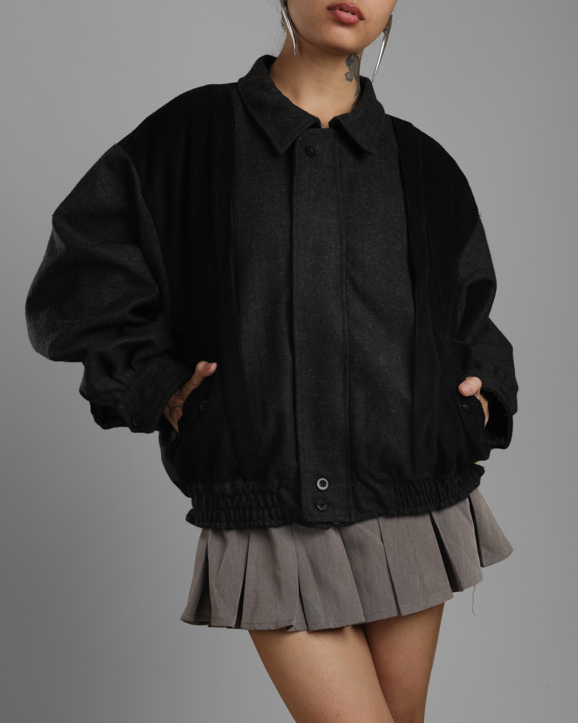 person wearing a black grey wood corduroy zipper jacket with collar and grey skater skirt against a gray background
