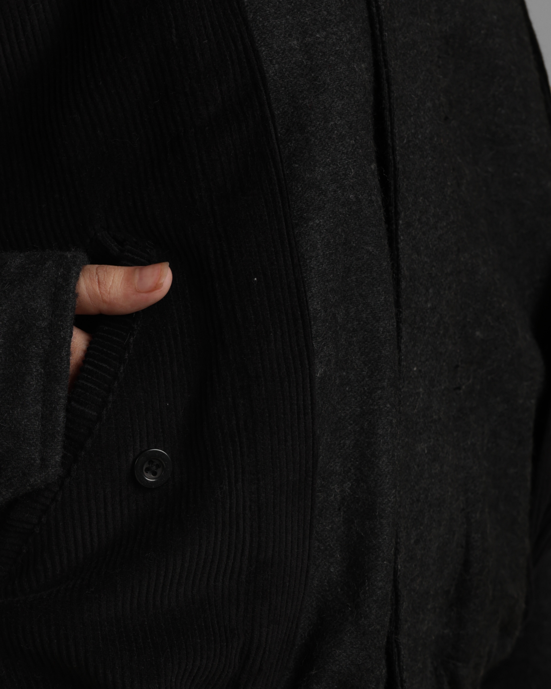 Close-up of a black coat with a button, held by a hand.