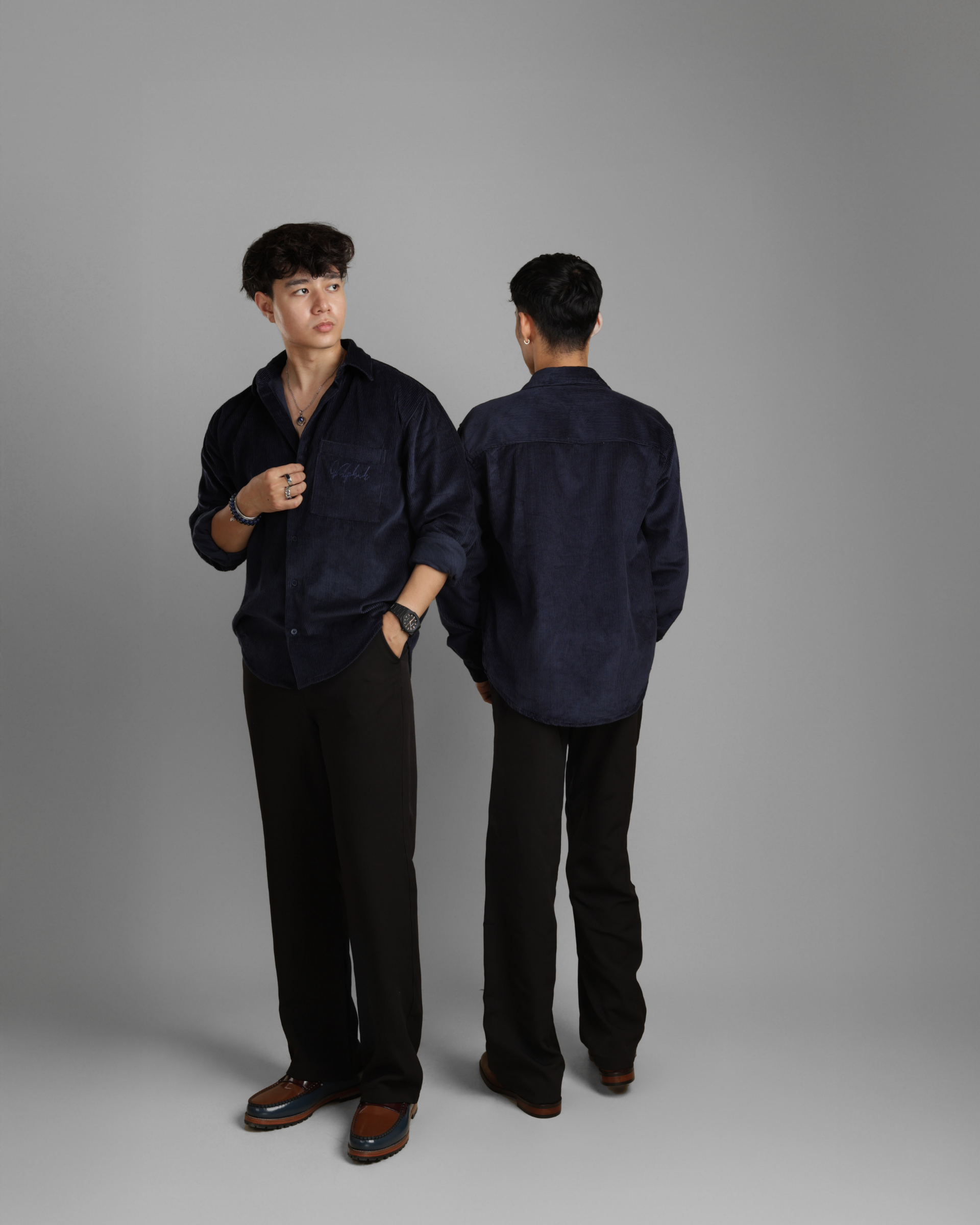 Men wearing a dark blue corduroy shirt and black pants against a gray background