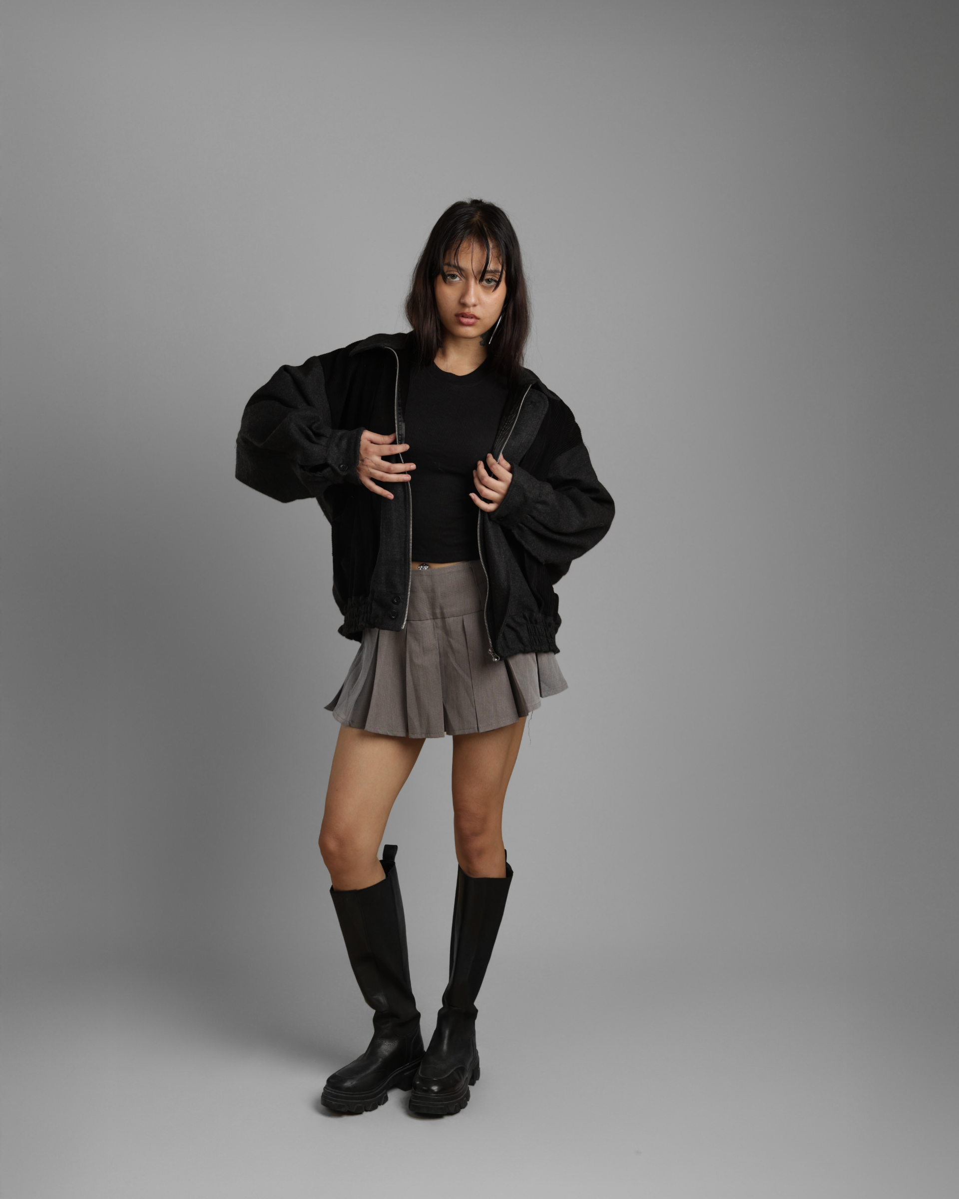 person wearing a black grey wood corduroy zipper jacket with collar and grey skater skirt against a gray background