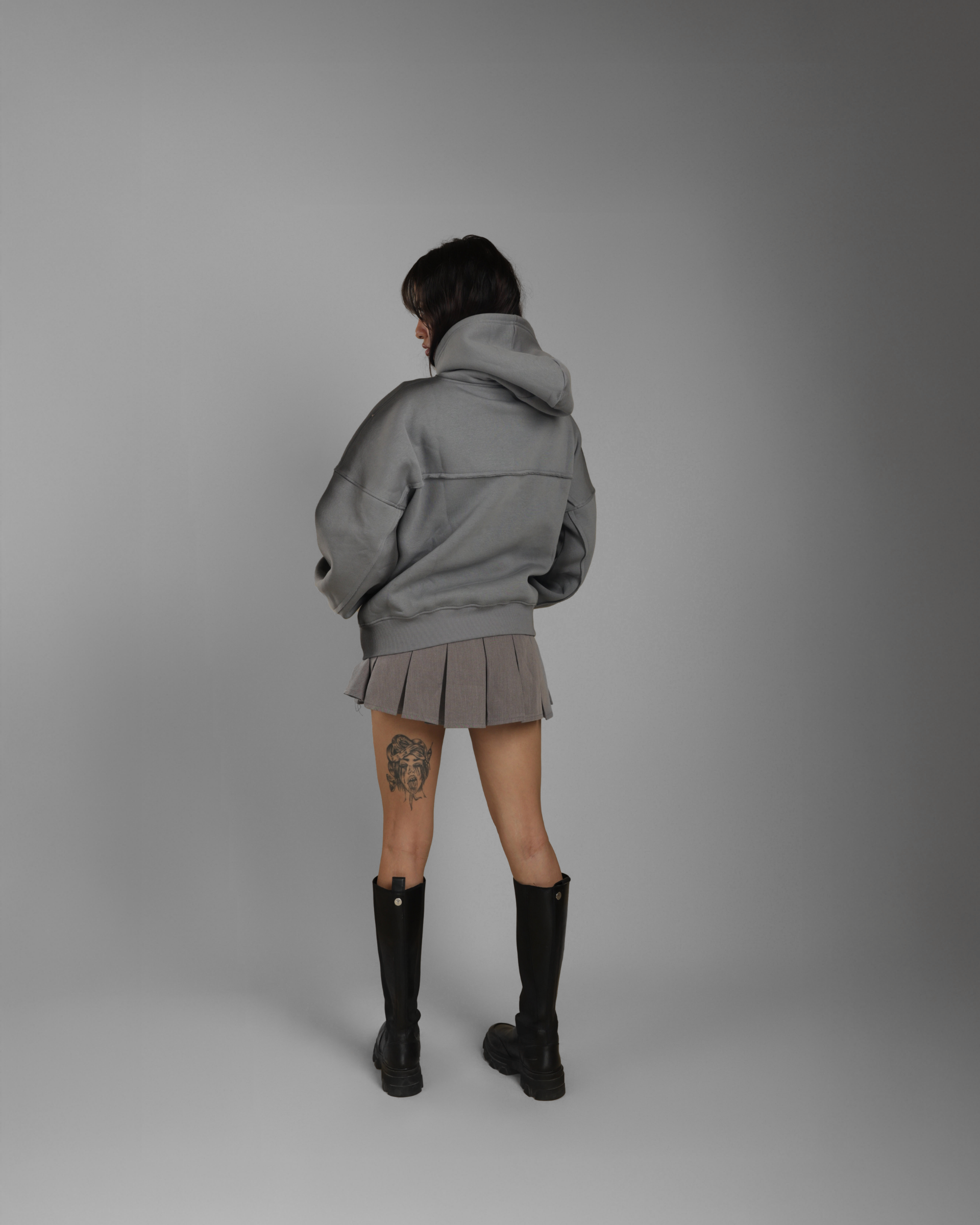 Person wearing a gray hoodie, skirt, and black boots on a plain background