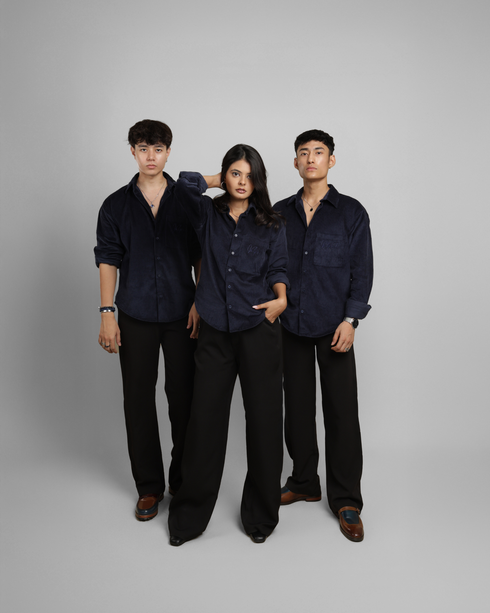 three people wearing a dark blue corduroy shirt and black pants against a gray background