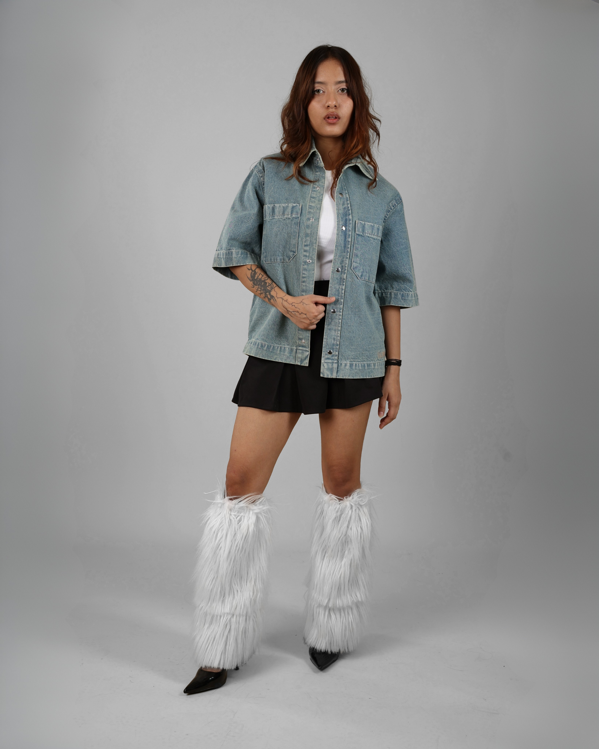 Person wearing a denim jacket, black skirt, and white fringed boots on a gray background