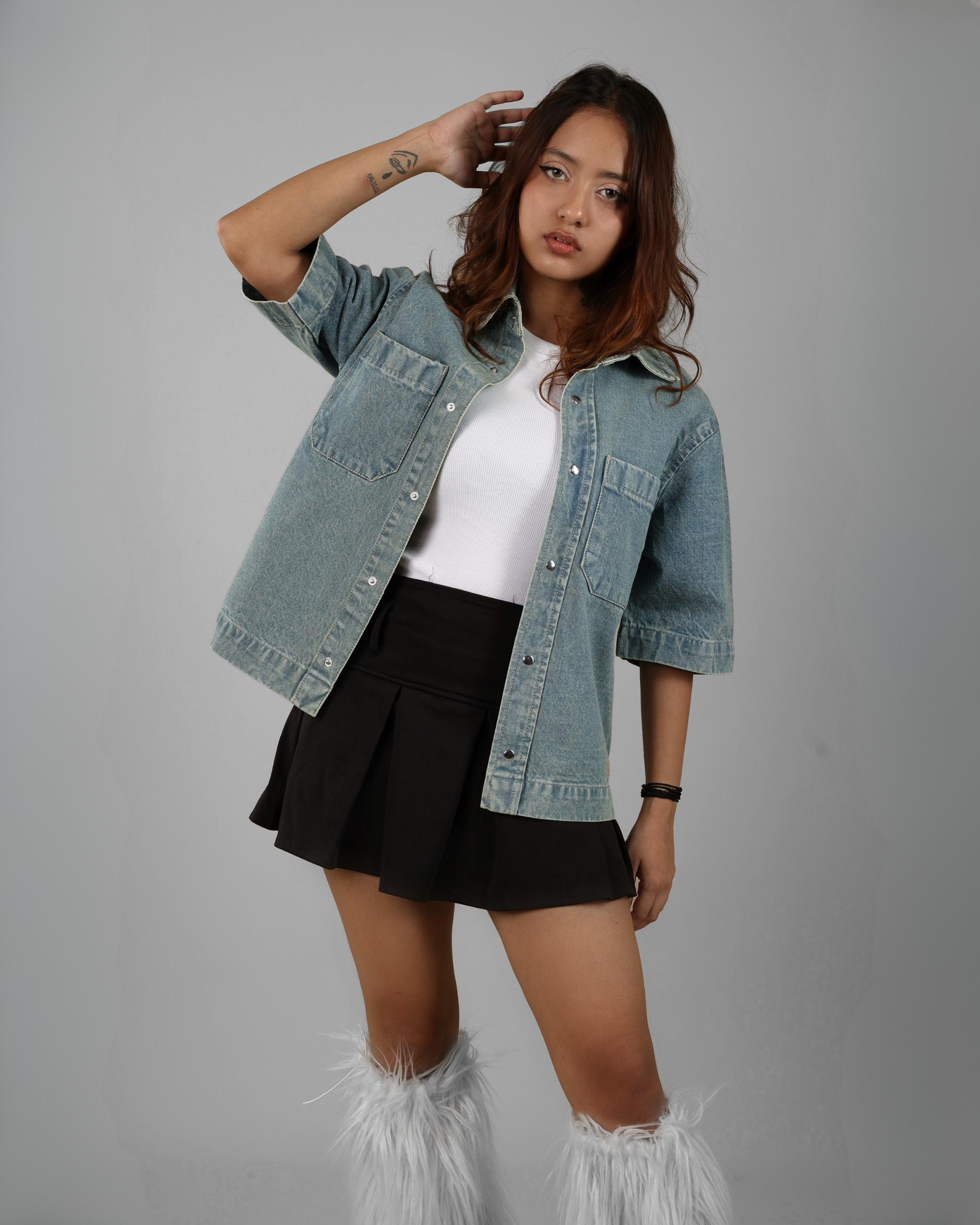 Woman wearing a denim jacket, white top, black skirt, and white boots on a gray background