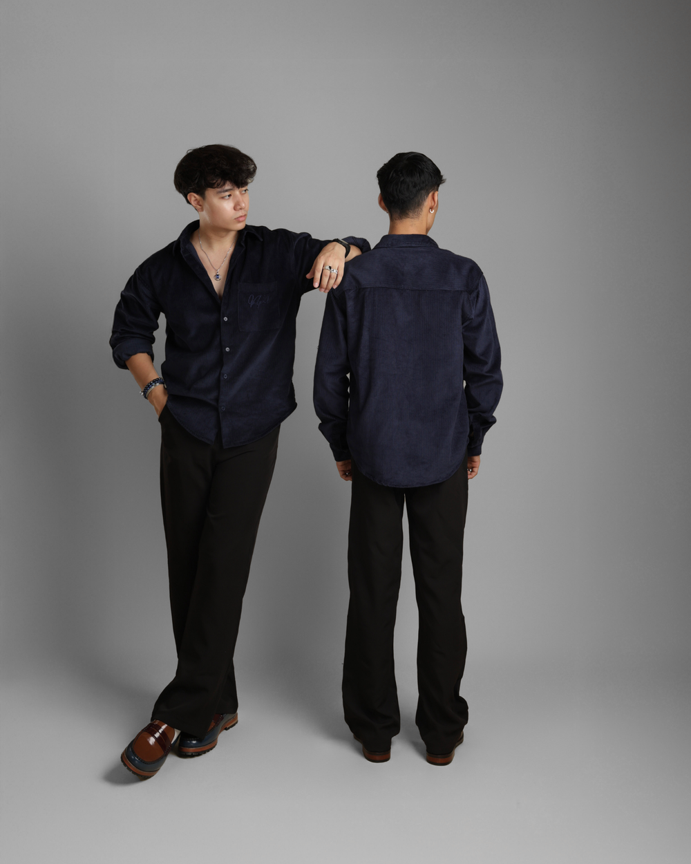 Person wearing a dark shirt and pants, standing against a gray background.