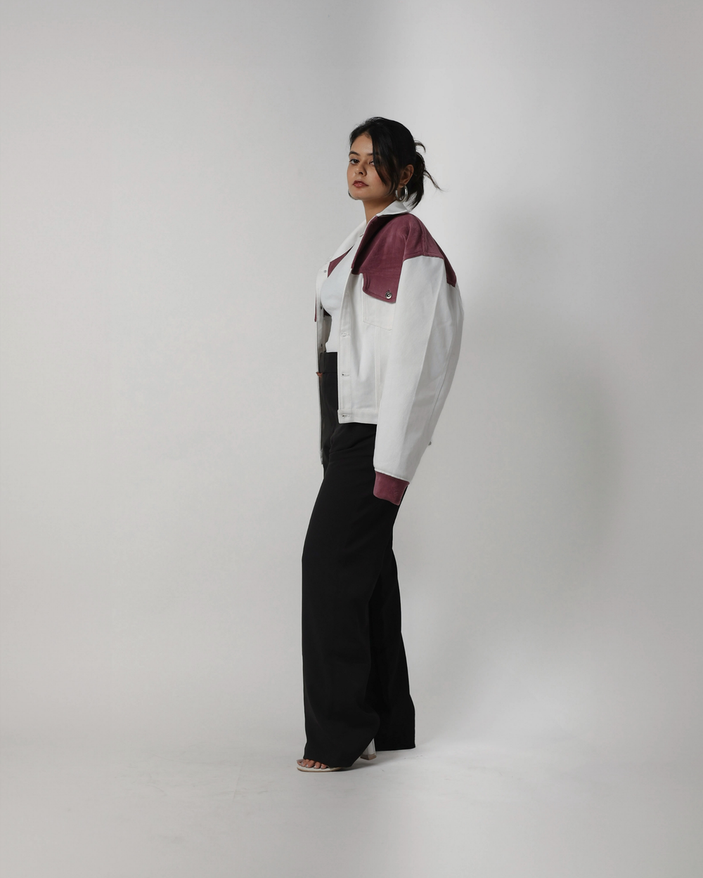 Person wearing a modern outfit with a white and onion pink jacket and black pants on a plain background