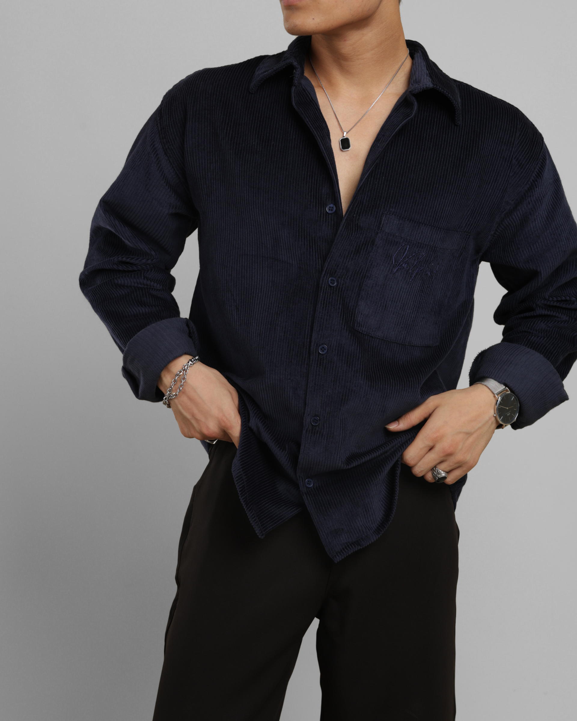 Man wearing a dark blue corduroy shirt and black pants against a gray background