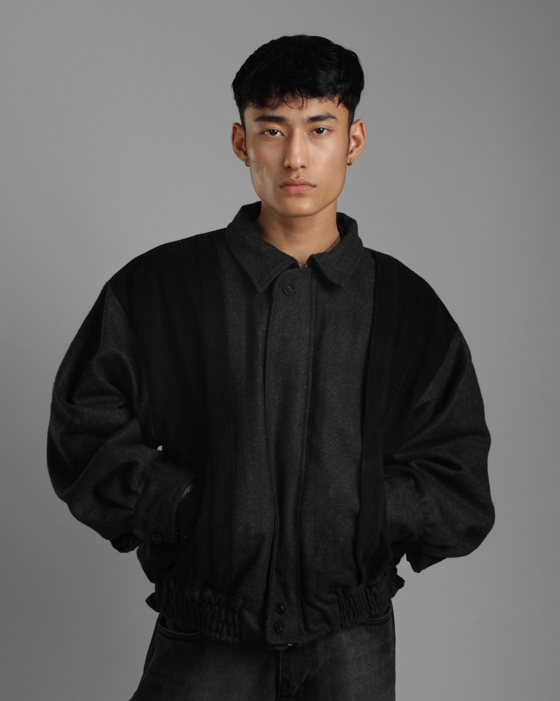 Man wearing a black grey wood corduroy zipper jacket with collar and black jeans against a gray background