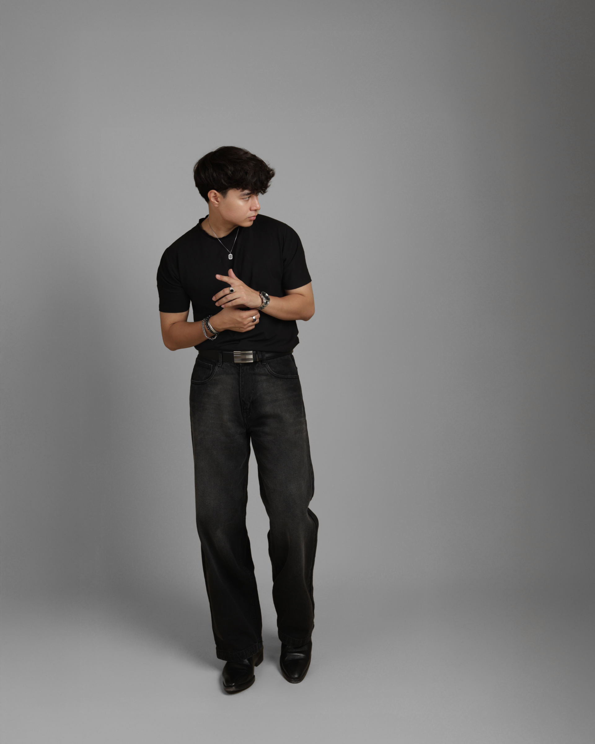 man wearing black outfits including black denims standing against a gray background