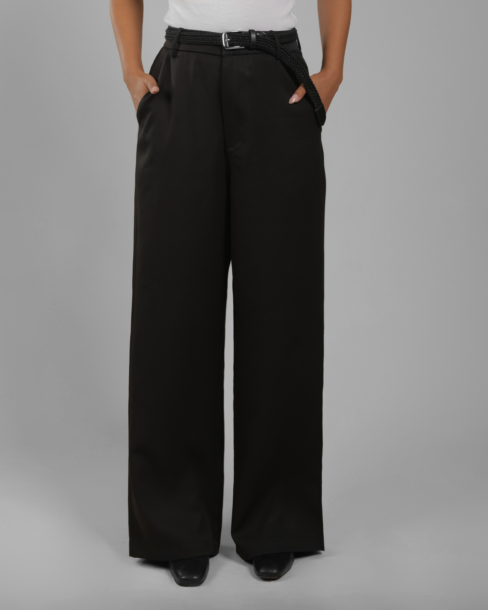 A person wearing black wide-leg trousers with a matching black belt, standing against a plain gray studio background.