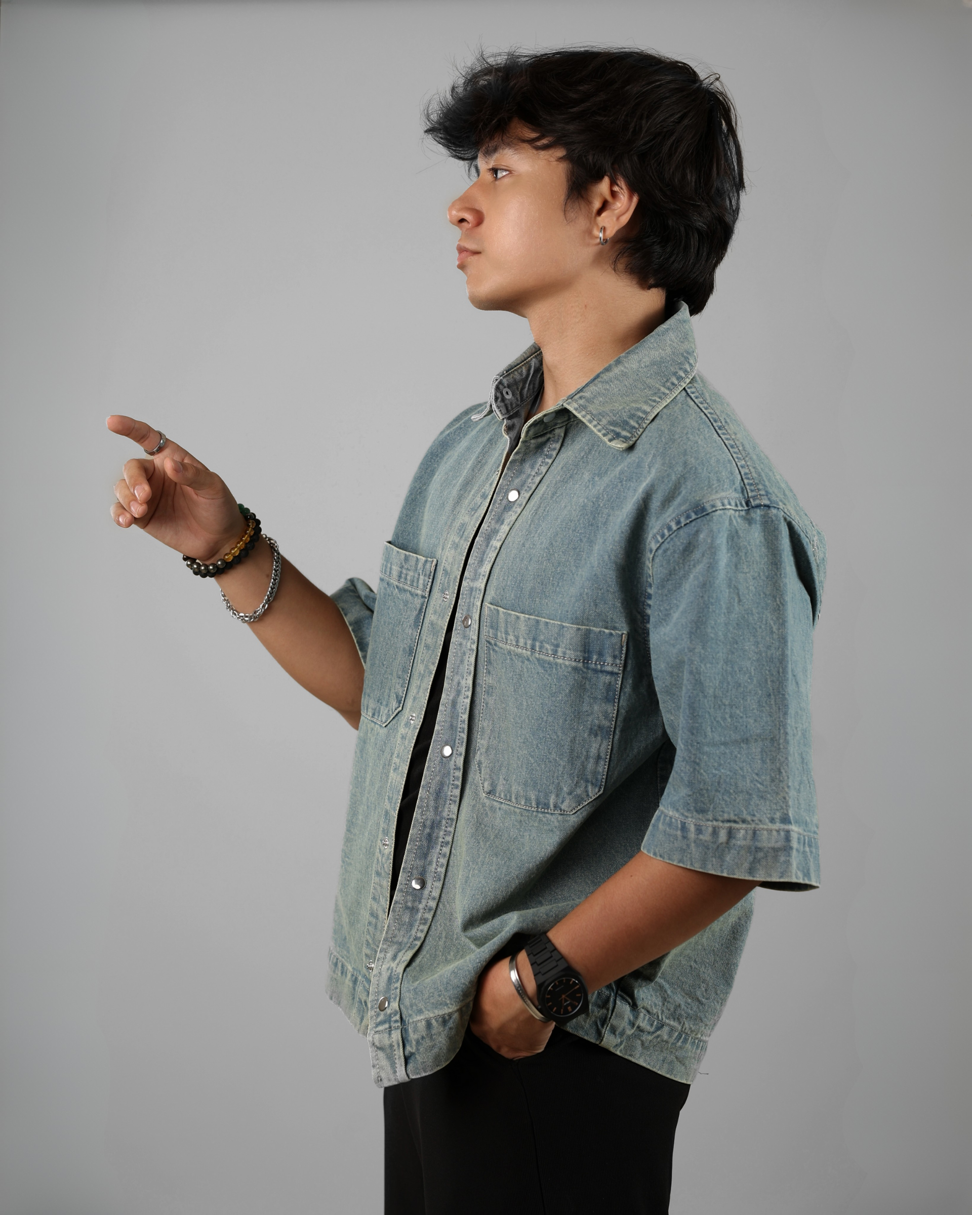 Person wearing a denim jacket pointing to the side against a gray background