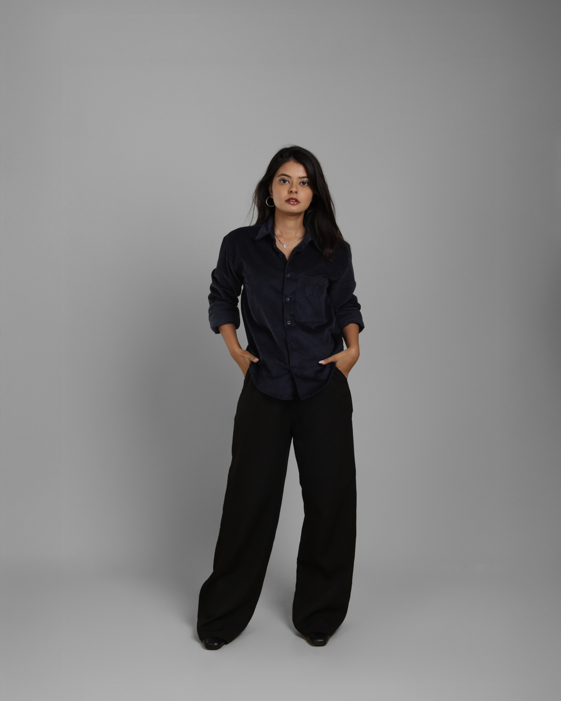 Woman wearing a dark blue corduroy shirt and black pants against a gray background