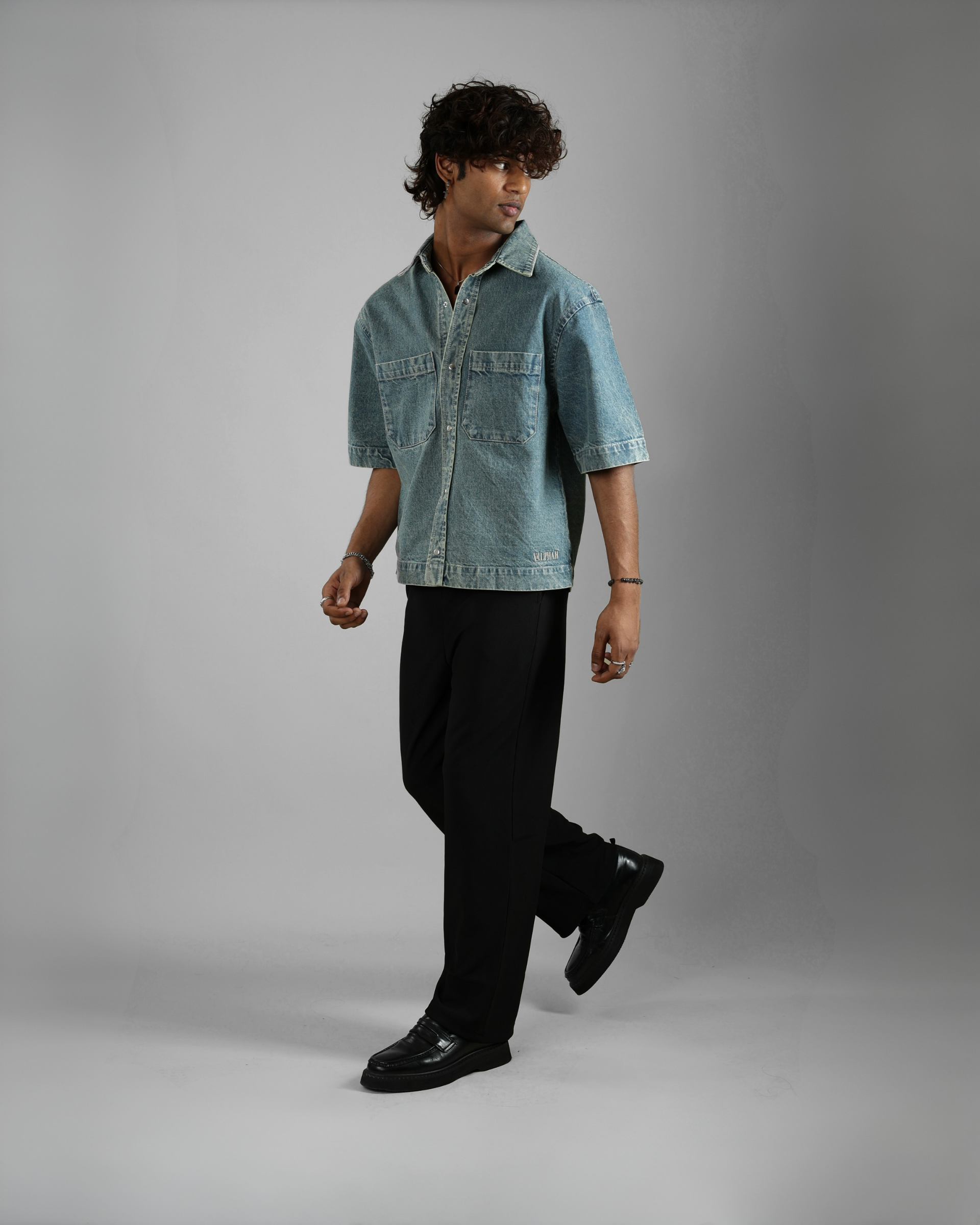 Man wearing a light blue denim shirt over a black outfit on a gray background