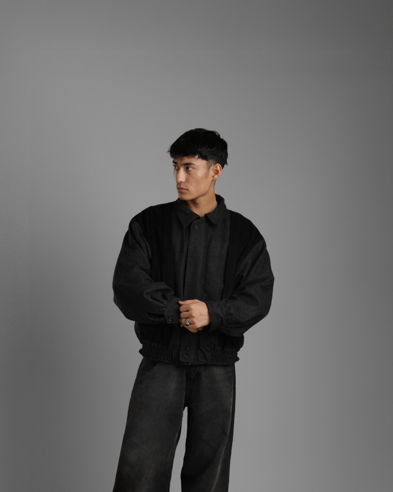 Person wearing a black jacket and pants against a gray background