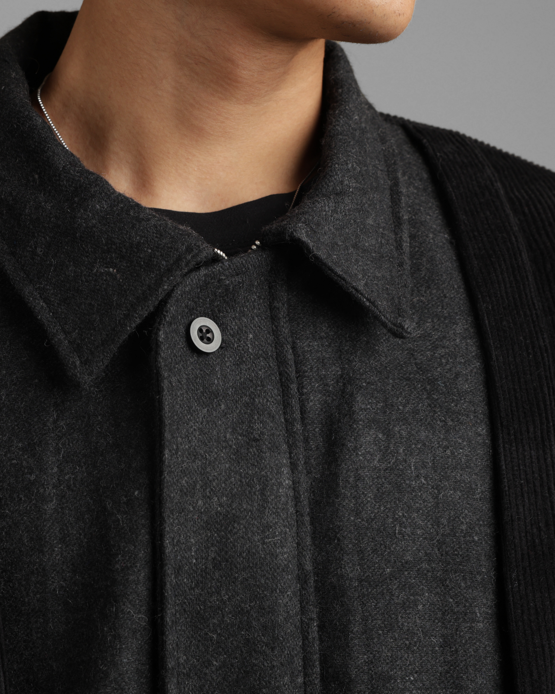 Close-up of a dark gray coat zipper jacket with a button on a neutral background