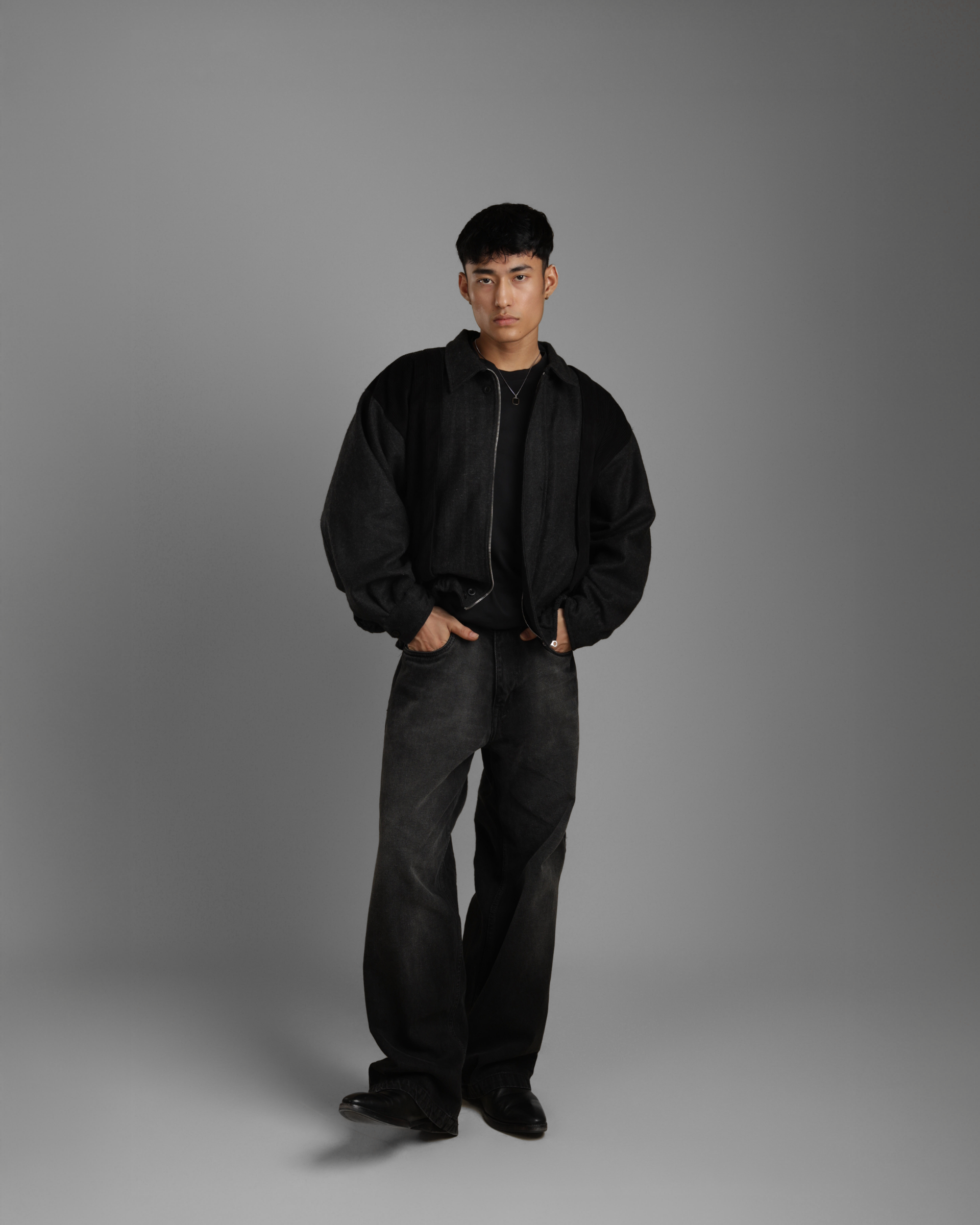 person wearing a black grey wood corduroy zipper jacket with collar and black jeans against a gray background