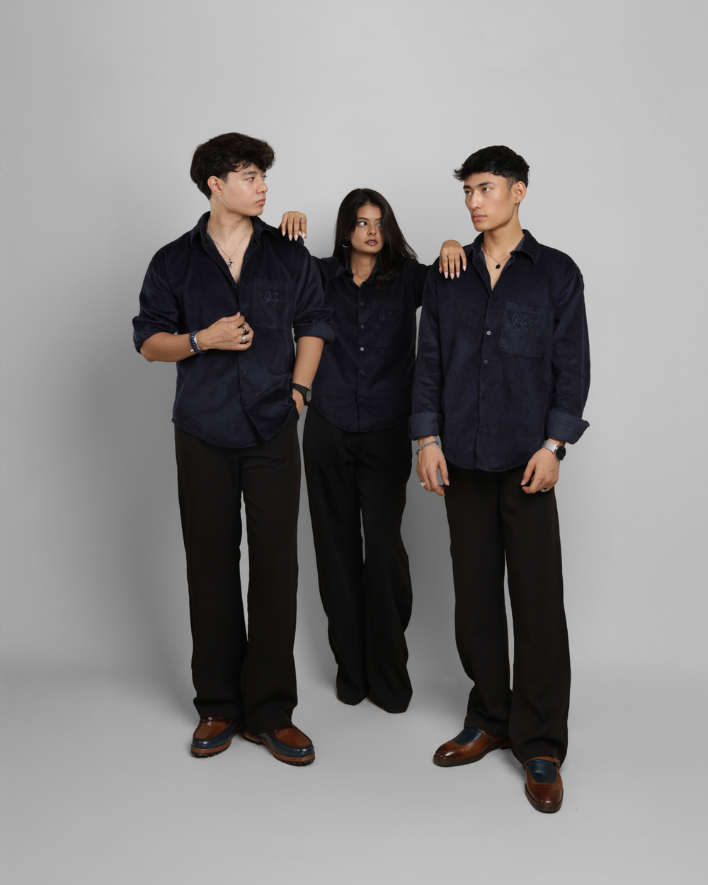 Three individuals wearing matching dark shirts and pants against a plain background