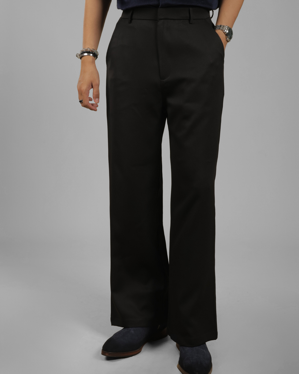 A person wearing black wide-leg trousers, styled with a dark navy top and dark suede boots, photographed against a neutral gray studio background.
