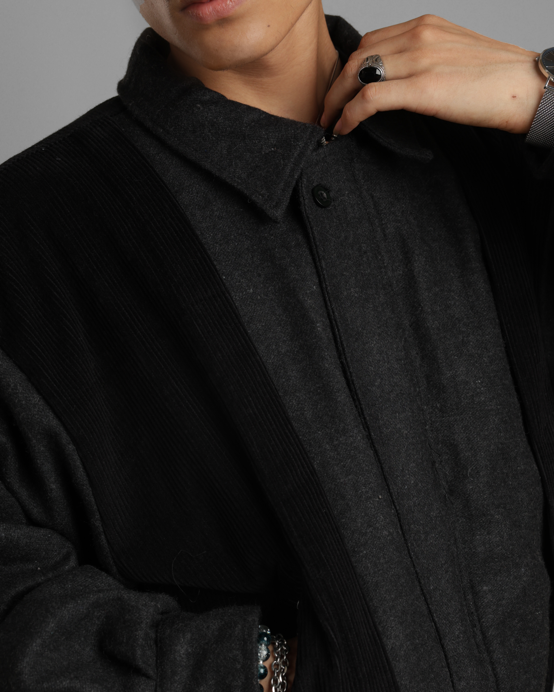 Close up of a person wearing a black grey wood corduroy zipper jacket with collar and black jeans against a gray background