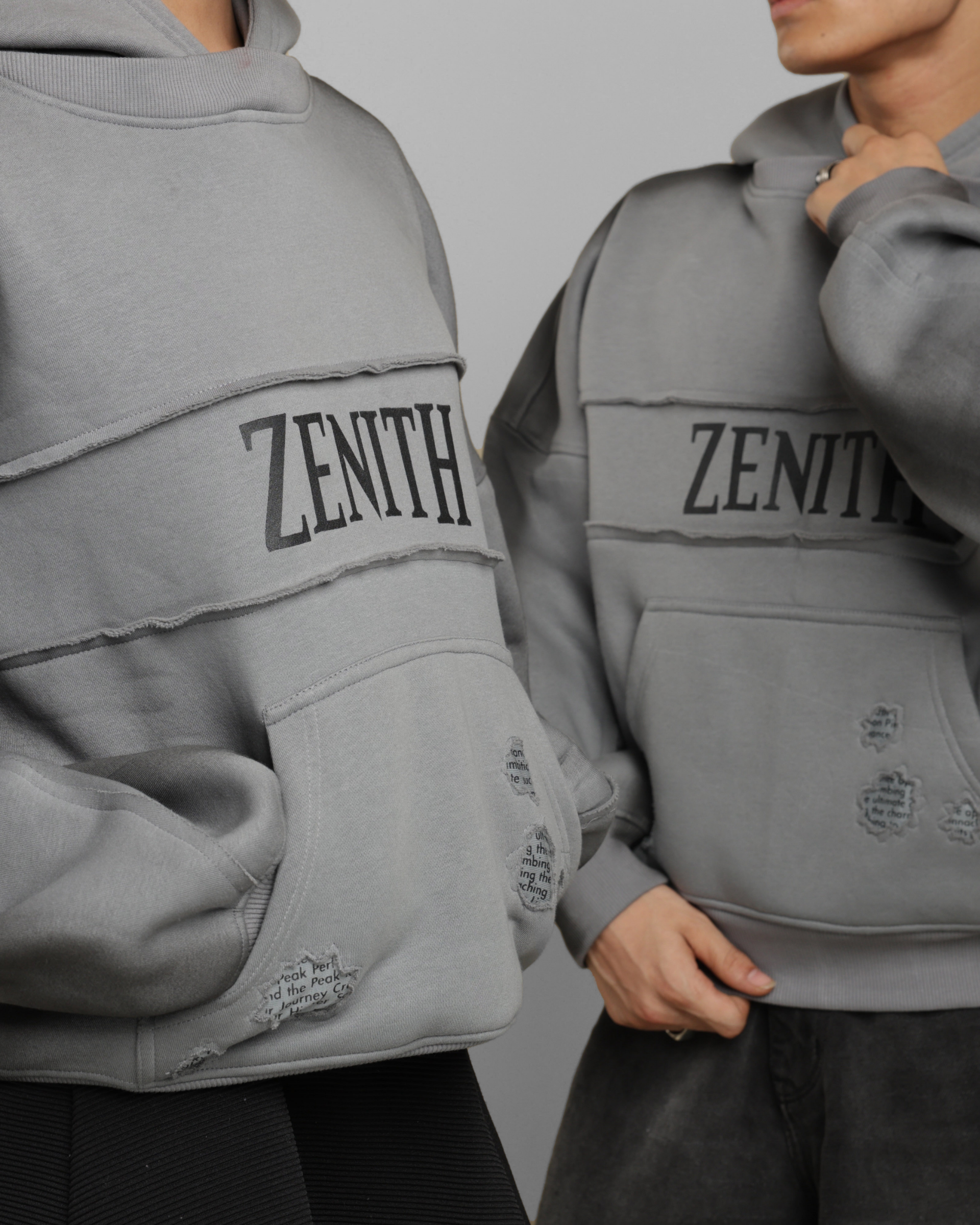 Two people wearing gray hoodies with 'ZENITH' branding on a plain background