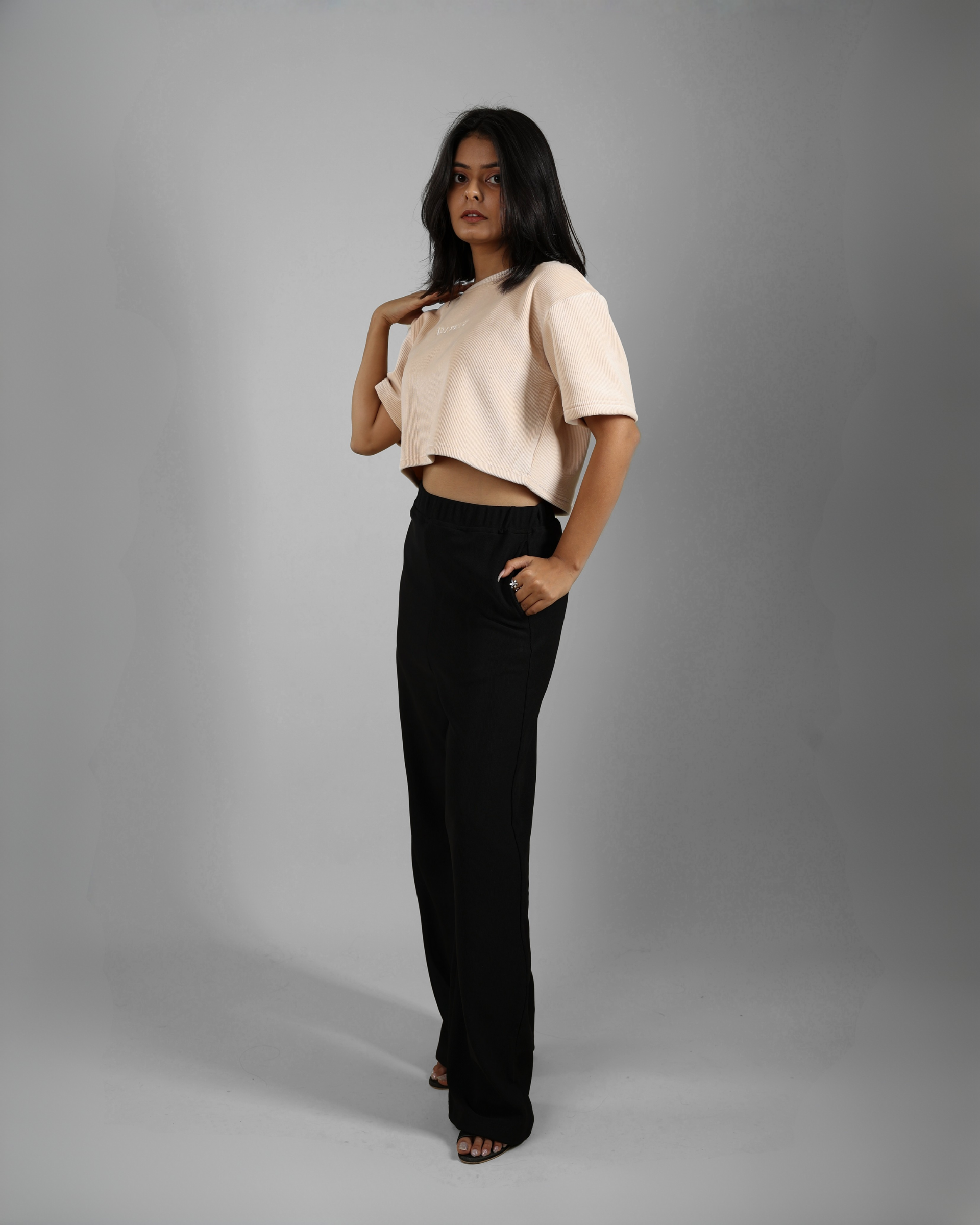 Woman wearing a beige top and black pants against a gray background