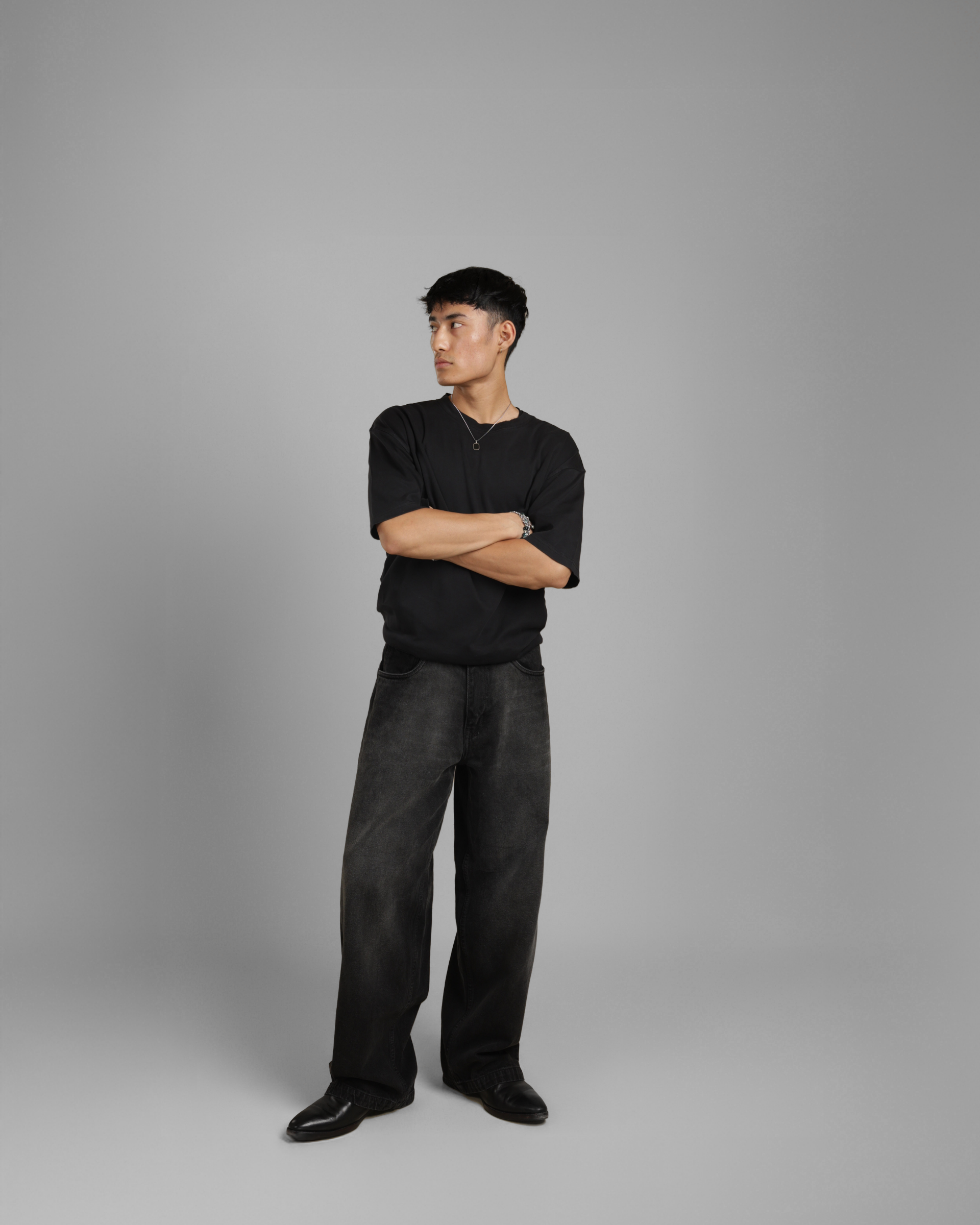 Man wearing a black shirt and dark pants against a gray background
