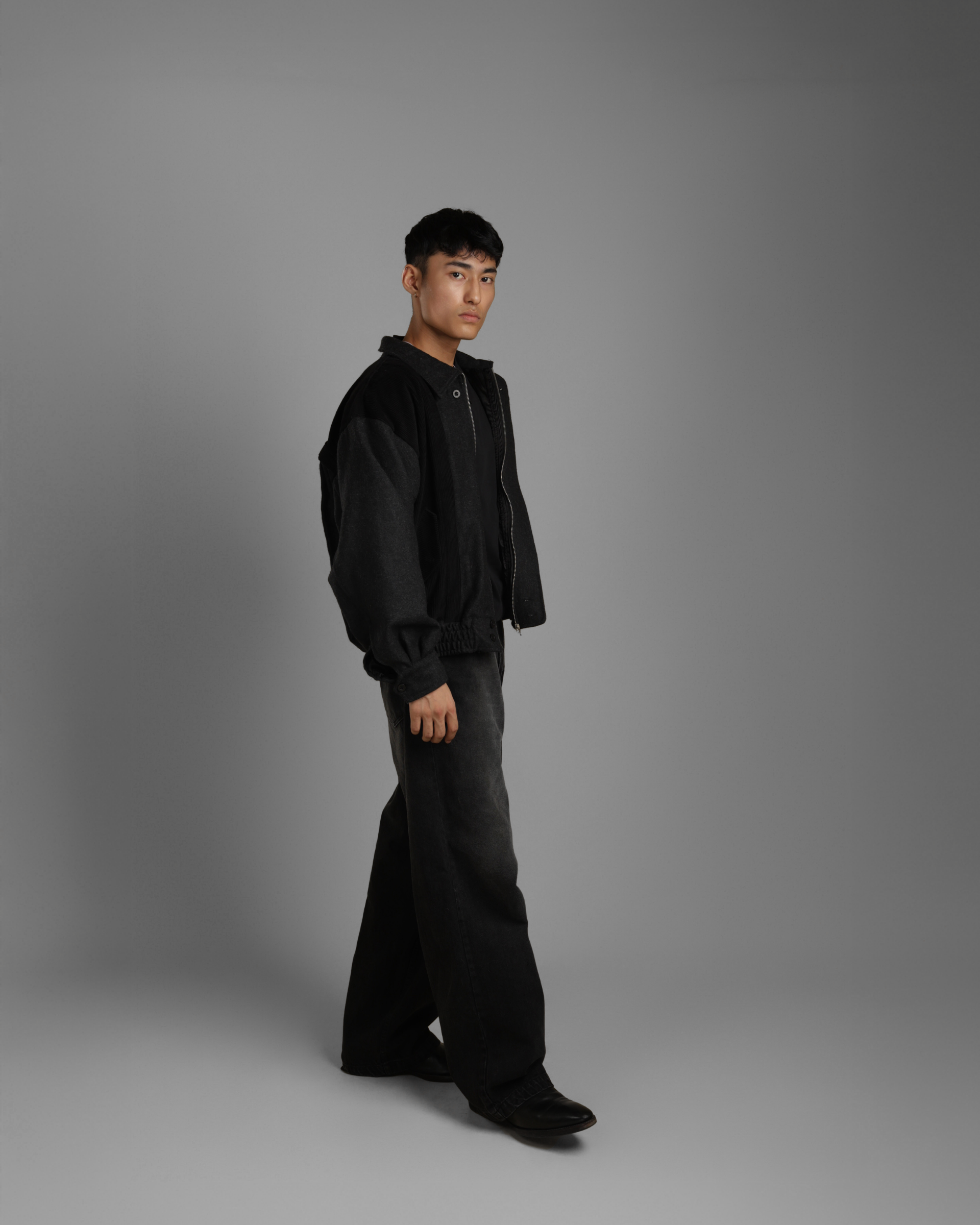 person wearing a black grey wood corduroy zipper jacket with collar and black jeans against a gray background