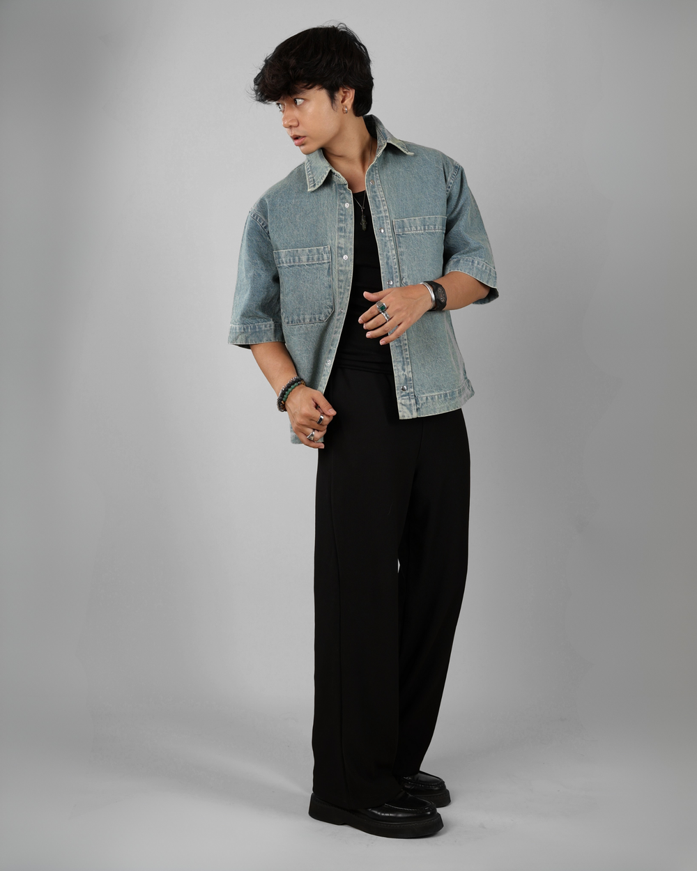 Person wearing a light blue denim jacket over a black shirt and pants on a gray background
