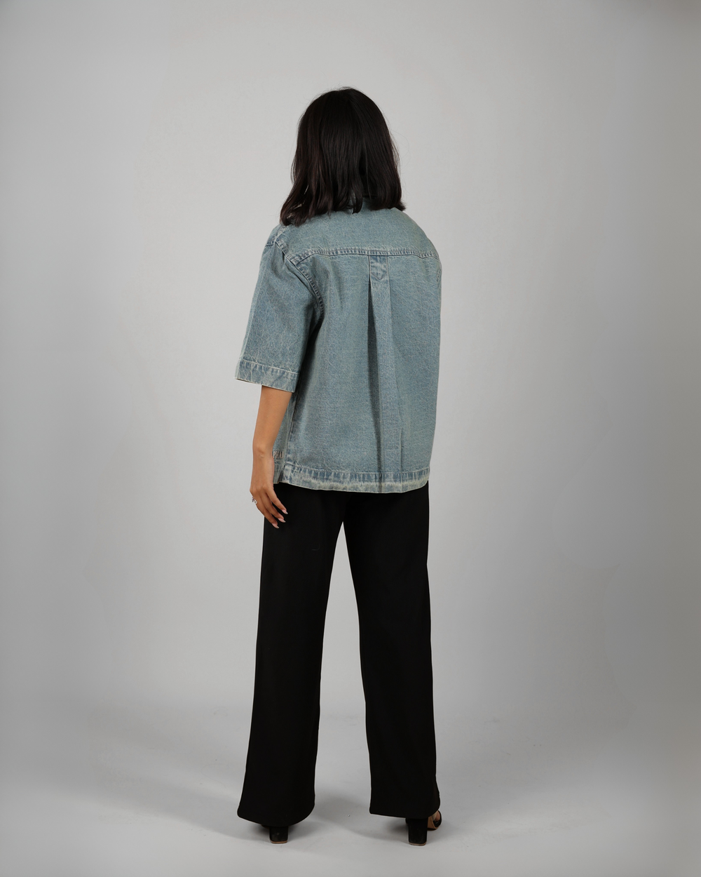 Person wearing a denim jacket and black pants on a gray background