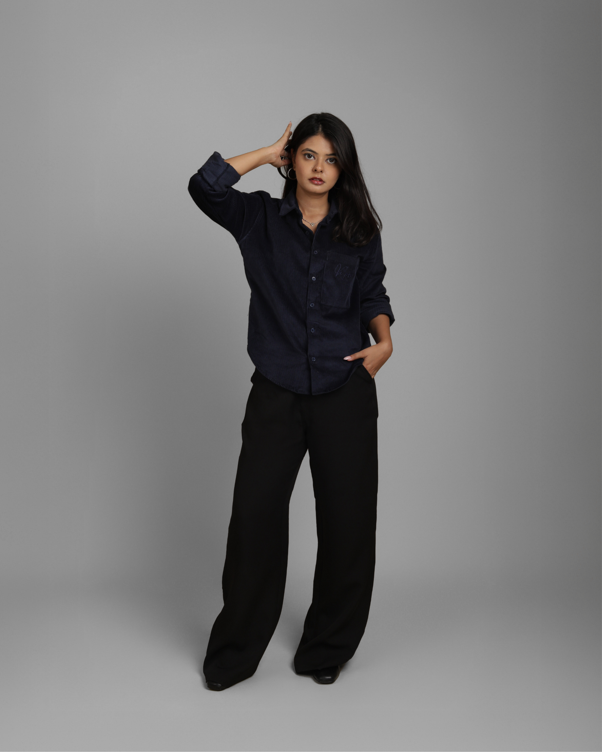 Woman wearing a dark blue corduroy shirt and black pants against a gray background