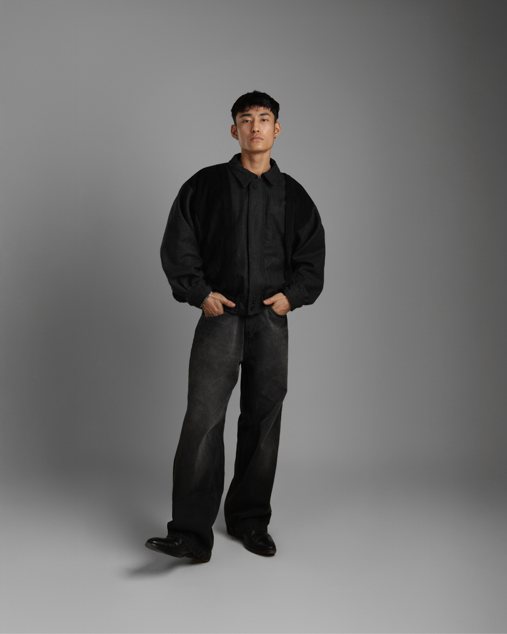 Man wearing a black grey wood corduroy zipper jacket with collar and black jeans against a gray background