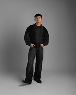 Man wearing a black grey wood corduroy zipper jacket with collar and black jeans against a gray background