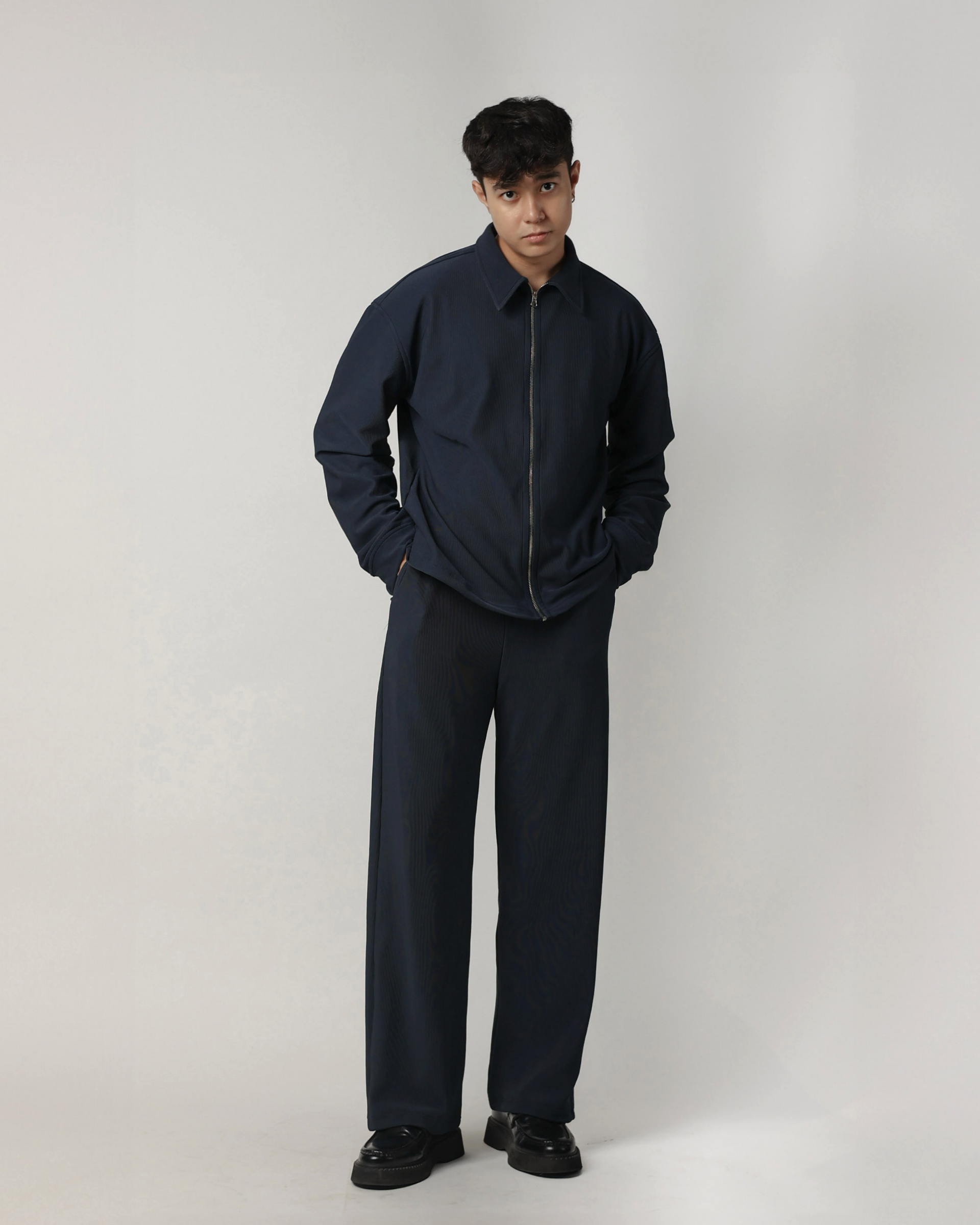 Person wearing a charcoal blue shacket and pants on a white background