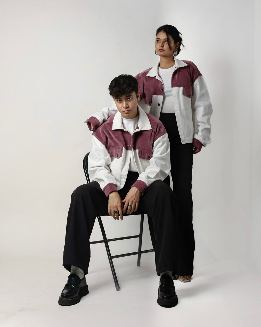 Two people wearing matching jackets sitting on a white background