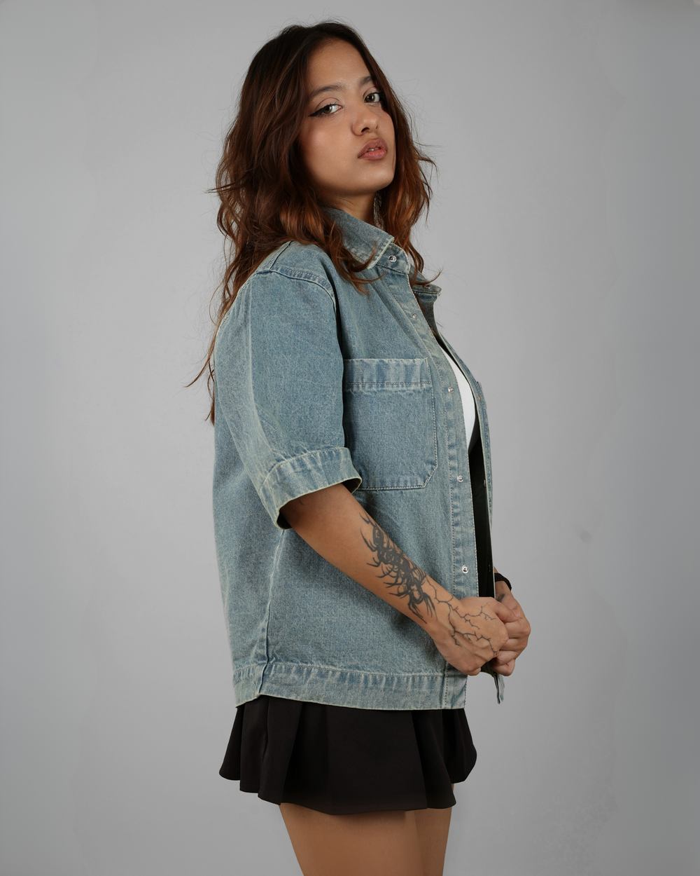 Woman wearing a denim jacket and black skirt against a gray background