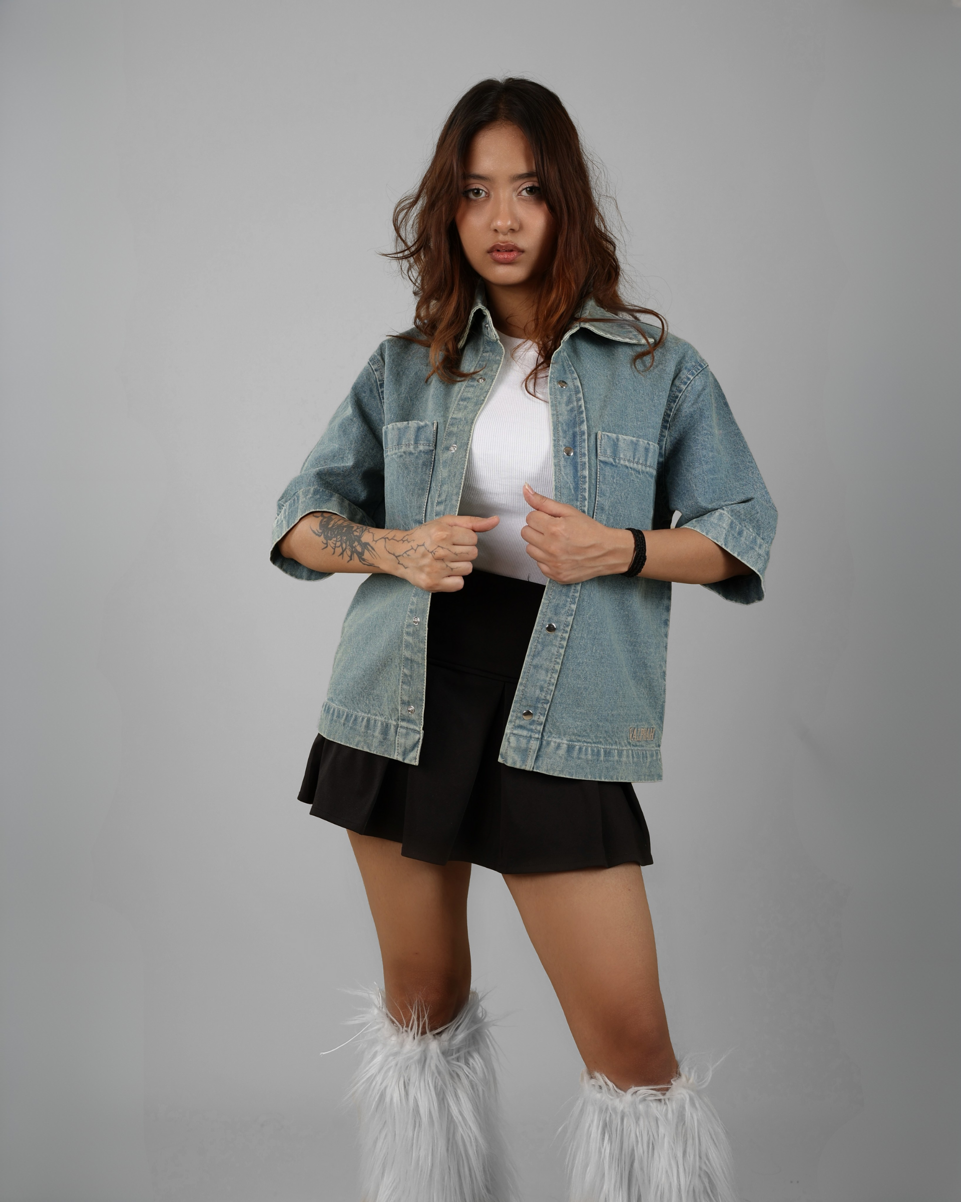 Woman wearing a denim jacket over a white shirt and black skirt on a gray background