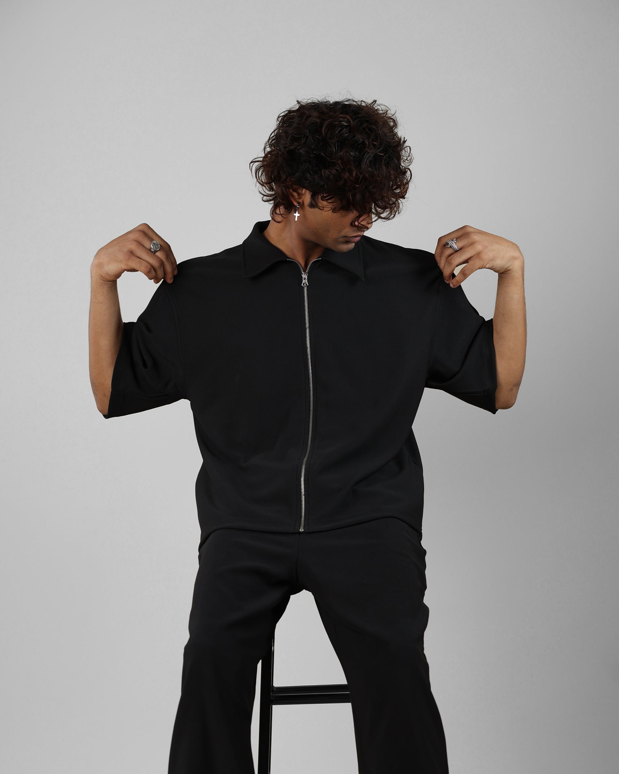 Person wearing a black outfit sitting on a stool against a gray background